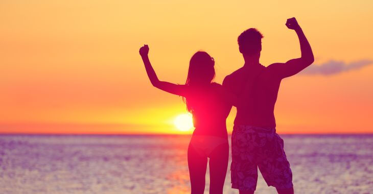 Happy energetic fit couple watching a sunset on the beach