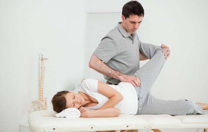 A woman undergoing hip joint mobilization therapy at an osteopath office.
