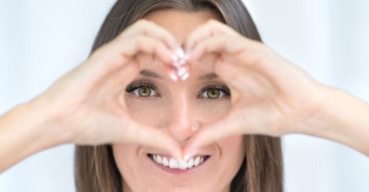 A happy woman with beautiful eyes forming a shape of heart with her hands in front of her face