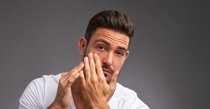 A concerned man watching looking at his eyes in a mirror.