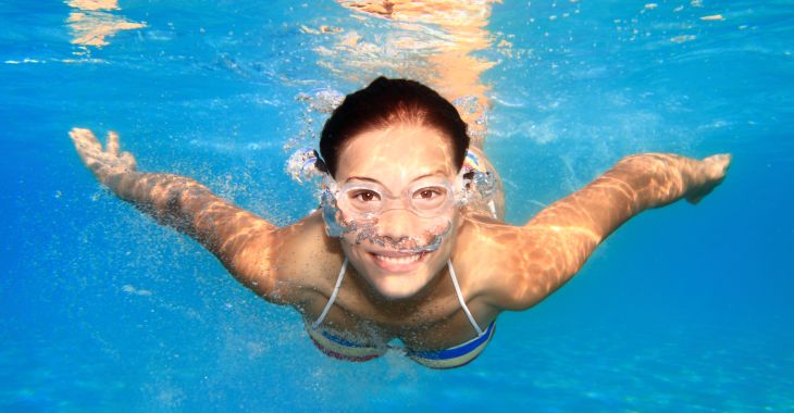 A smiling woman swimming underwater in a swimming pool. 