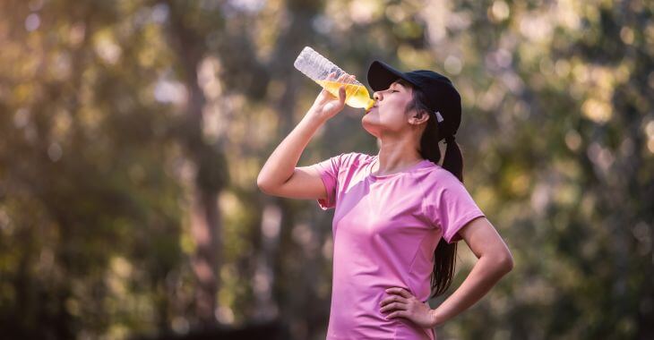 A sporty woman drinking electrolyte drink while getting activity outdoors.