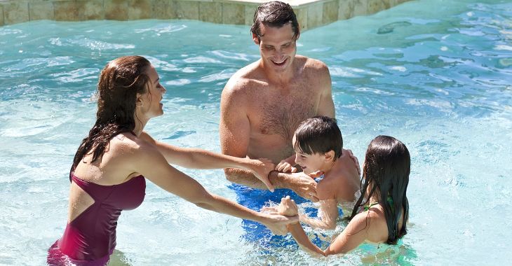 A mother and father having fun on vacation playing with their children in a swimming pool