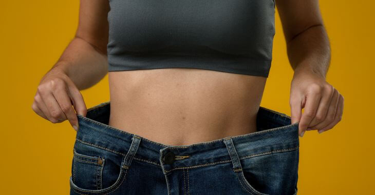 A woman after lipo body sculpting in a oversized old jeans 