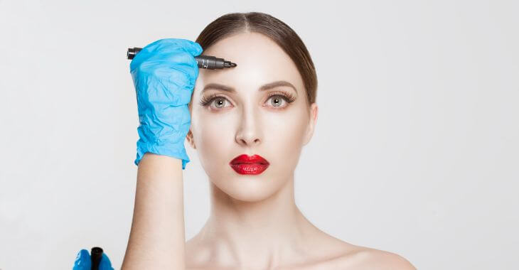 A plastic surgeon drawing marking lines on woman's forehead before forehead reduction surgery