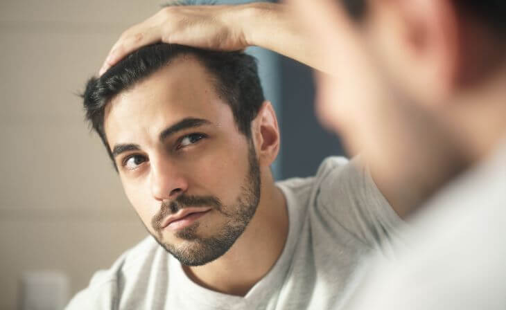 A handsome concerned man watching his hairline in a mirror. 