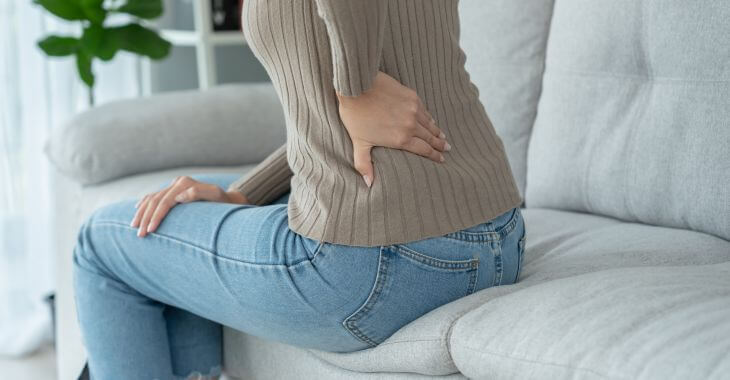 A woman with back pain caused by sciatica getting up from the sofa.