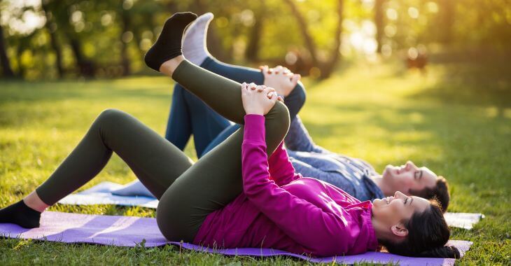 A couple doing exercises for sciatica recovery and spine stretching in a park.