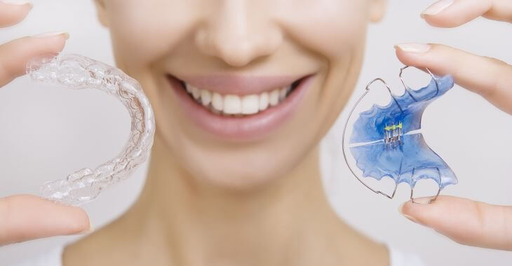 A woman with a perfect smile holding an invisible orthodontic braces in one hand and dental retainer in the other had