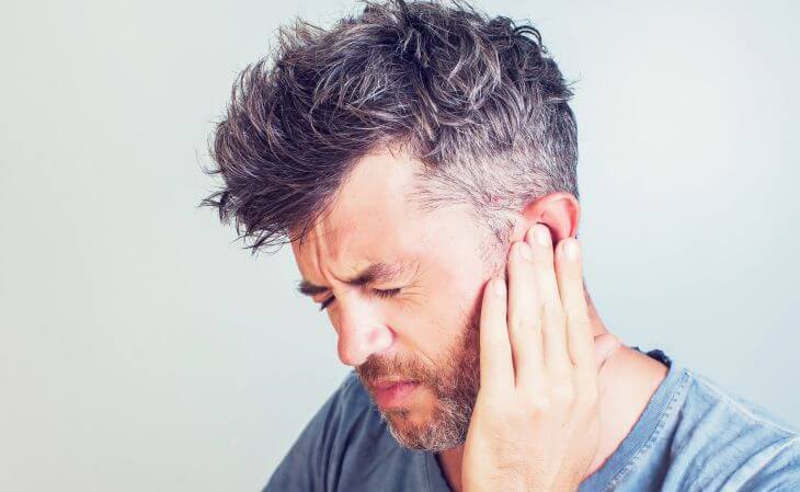 A man suffering from tinnitus pressing his left ear with his hand.