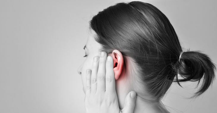 A woman feeling discomfort touching her left ear