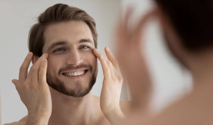 A happy handsome man after under-eye rejuvenation treatment looking his face and eyes