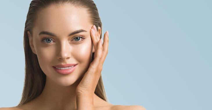 A face of a happy beautiful young woman touching skin on her temple